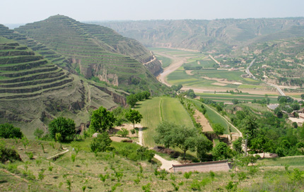 Terraced hillsides to the left and a valley with fields and roads below in rural China