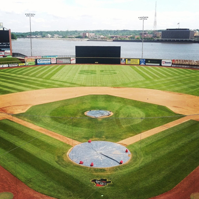 Baseball field for Iowa Quad City River Bandits features a mown baseball pattern around the pitcher's mound , the number 85 in the outfield, and stripes leading away from the 2nd and 3rd baselines.