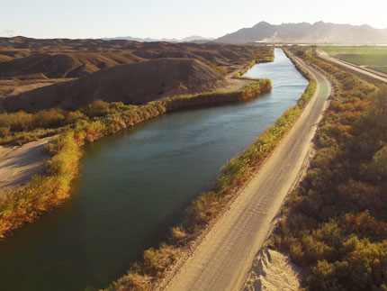 long irrigation ditch filled with water along roadside - mountains in distance