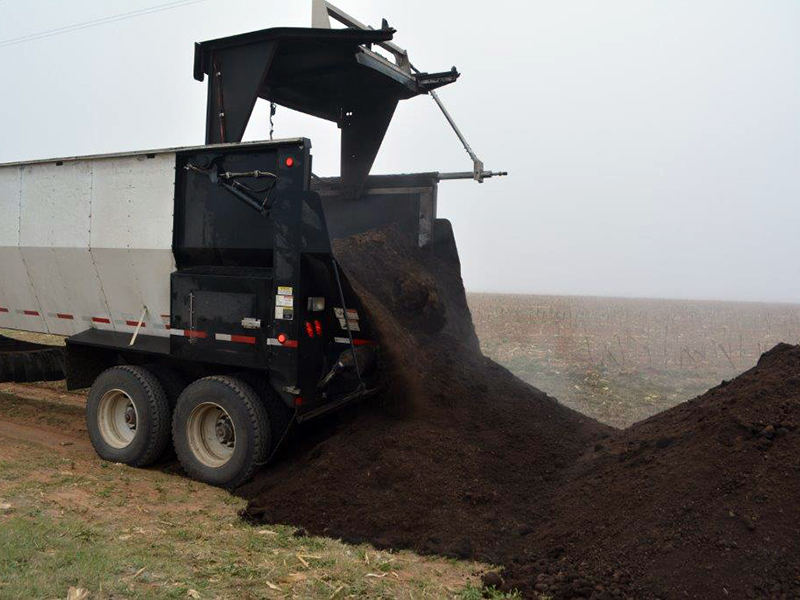 dumptruck dumping compost onto the ground in a field.