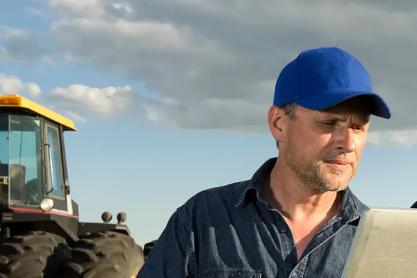 collaboration of two fieldworkers on a laptop with a tractor in the foreground